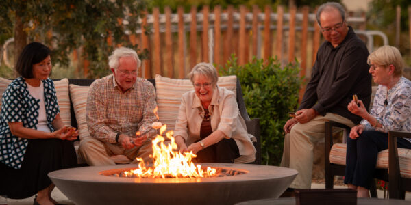 A photo of 5 residents sitting around the Paradise Valley Estates campfire - sharing chuckles and munching on some s'mores.